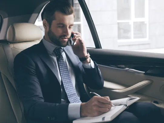 رجل في السيارة يتحدث على الهاتف ويكتب ملاحظات في دفتره