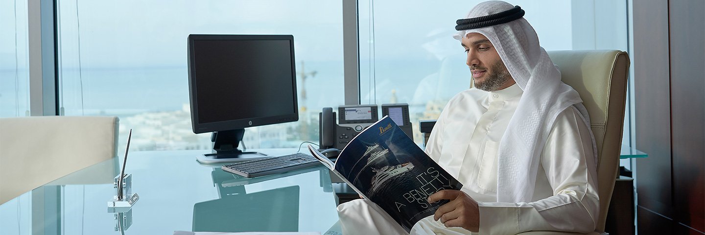 A businessman in Kuwait looking through a magazine about Boubyan's VISA Infinite Privilege in his workplace